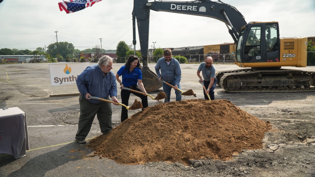 Four people use shovels to dig in a pile of dirt. 