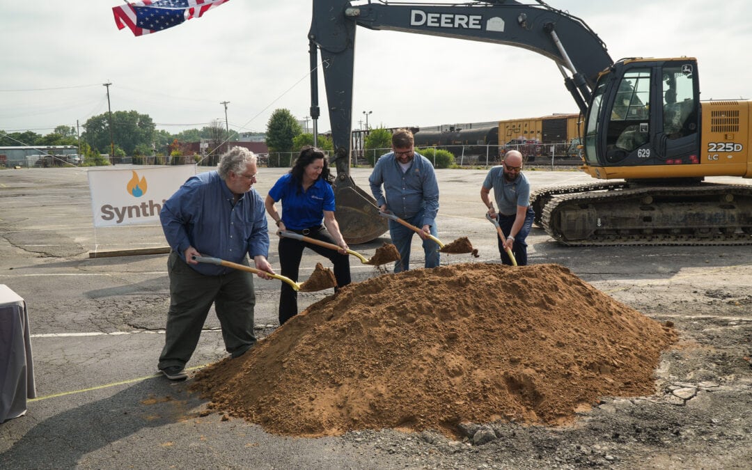 Four people dig into a pile of dirt with gold shovels.
